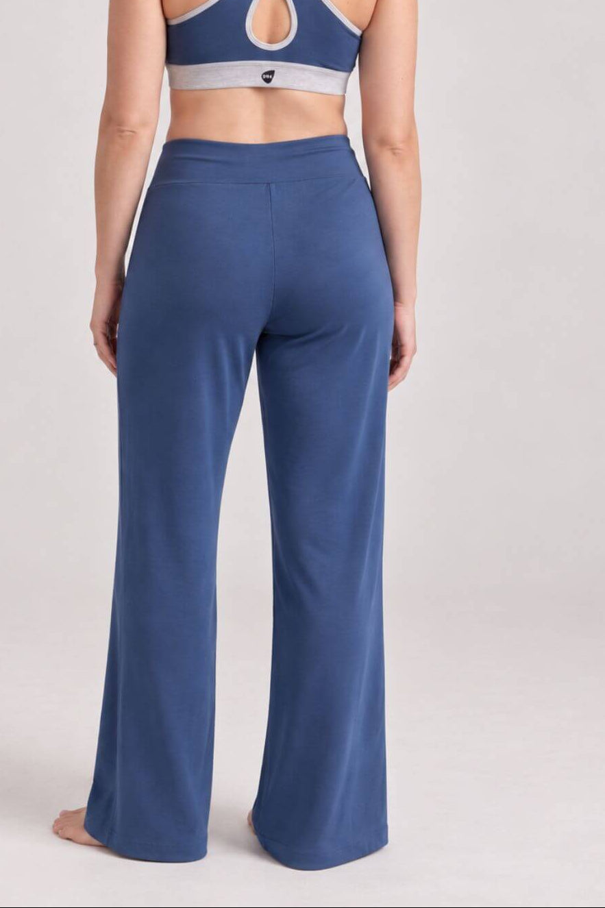 A woman shown from the back wearing a blue sports bra with a crossover crisscross back and matching blue wide-leg pants, photographed against a light gray studio background.