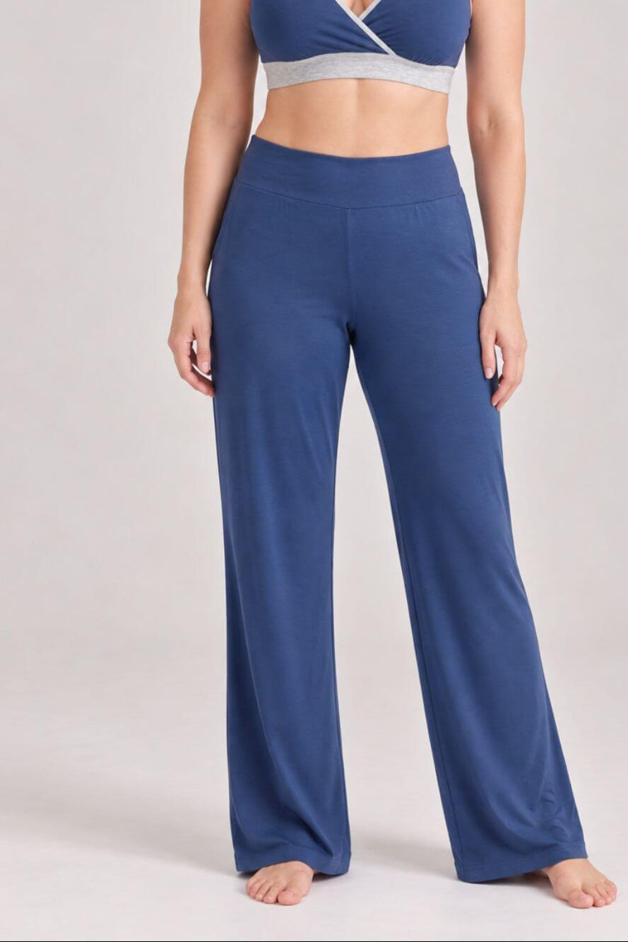 A woman modeling a matching two-piece loungewear set consisting of a blue wrap-style sports bra and high-waisted wide-leg pants, photographed against a neutral light gray studio 