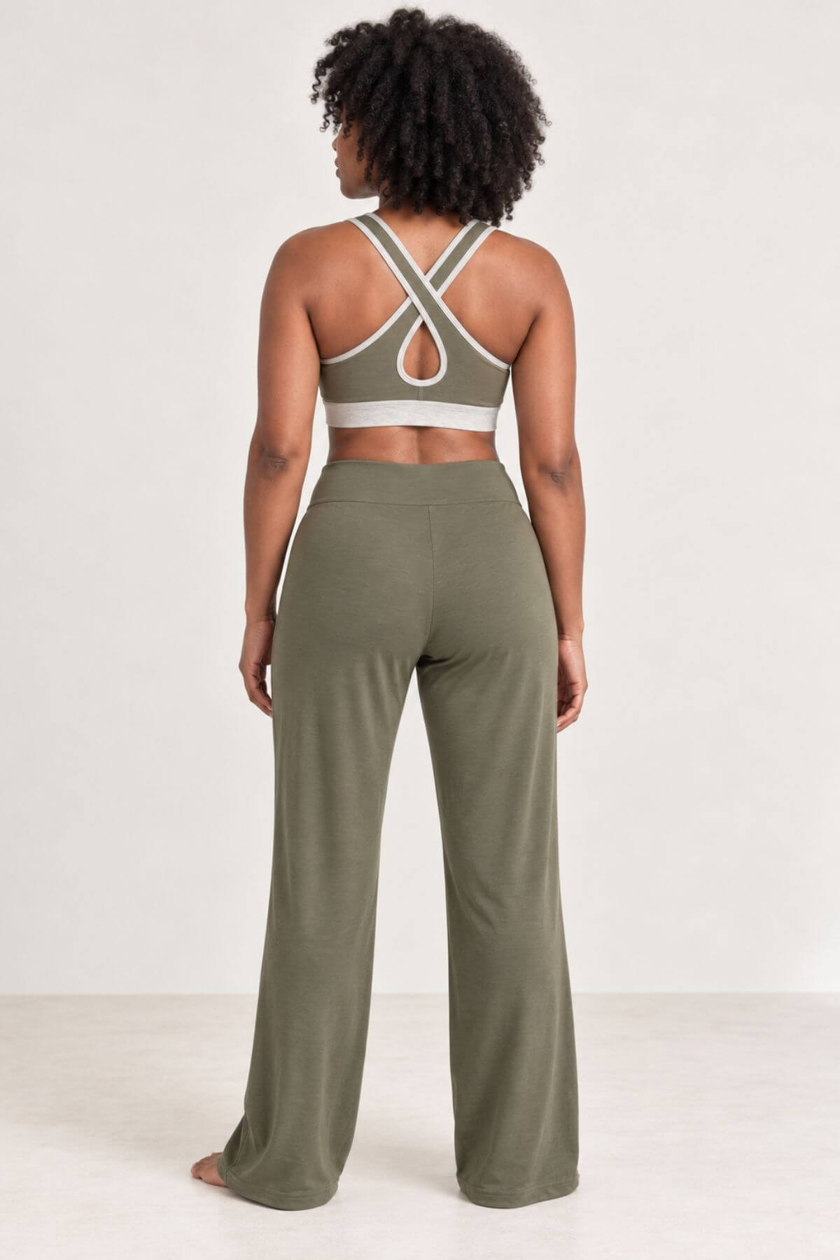 A woman shown from the back wearing an olive green two-piece activewear set, featuring a sports bra with crisscross straps and matching wide-leg pants, against a plain white studio background.