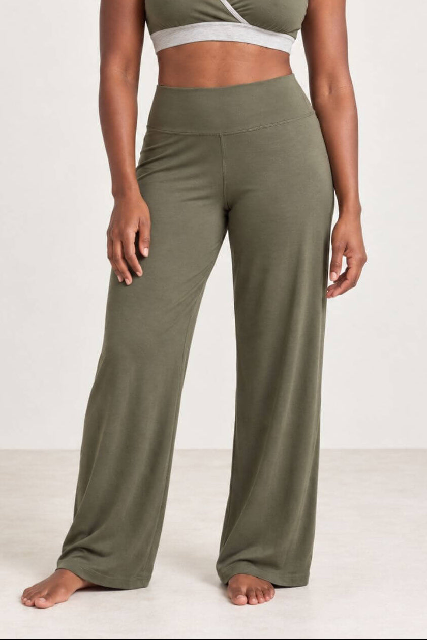 A woman modeling a matching olive green activewear set consisting of a wrap-style sports bra and high-waisted wide-leg pants, photographed against a plain off-white studio background.