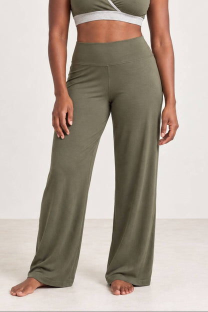 A woman modeling a matching olive green activewear set consisting of a wrap-style sports bra and high-waisted wide-leg pants, photographed against a plain off-white studio background.