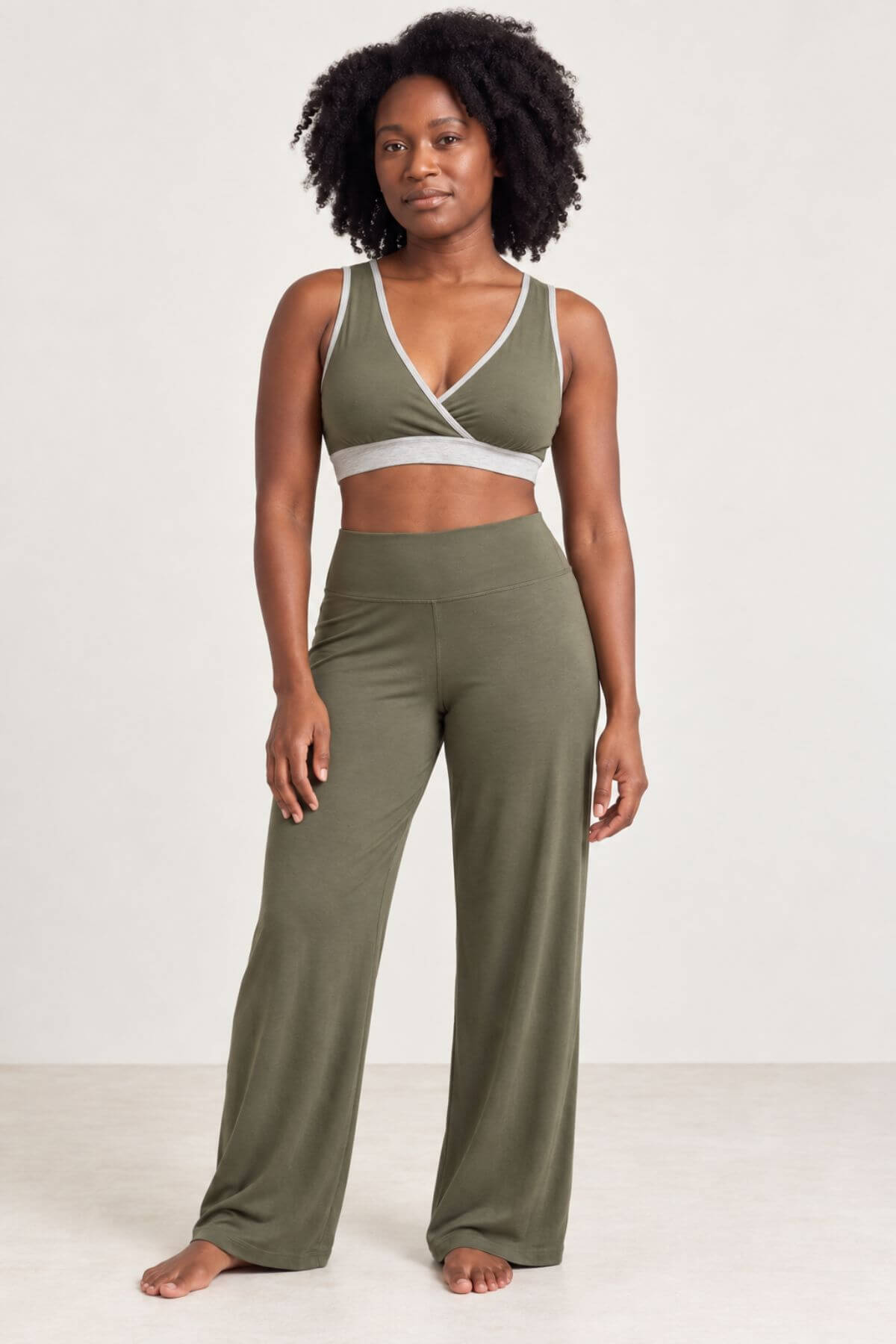 A woman modeling a matching olive green activewear set consisting of a wrap-style sports bra and high-waisted wide-leg pants, photographed against a plain off-white studio background.