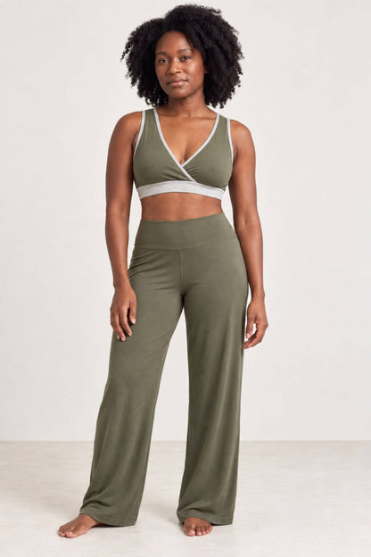 A woman modeling a matching olive green activewear set consisting of a wrap-style sports bra and high-waisted wide-leg pants, photographed against a plain off-white studio background.