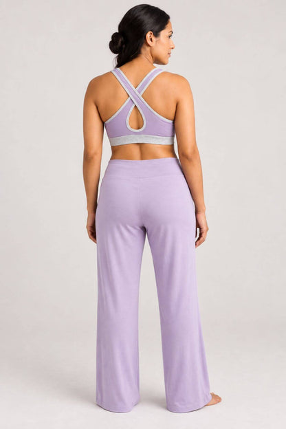 A woman shown from the back wearing a lavender two-piece activewear set consisting of a sports bra with crisscross straps and matching high-waisted wide-leg yoga pants, set against a plain light gray studio background.