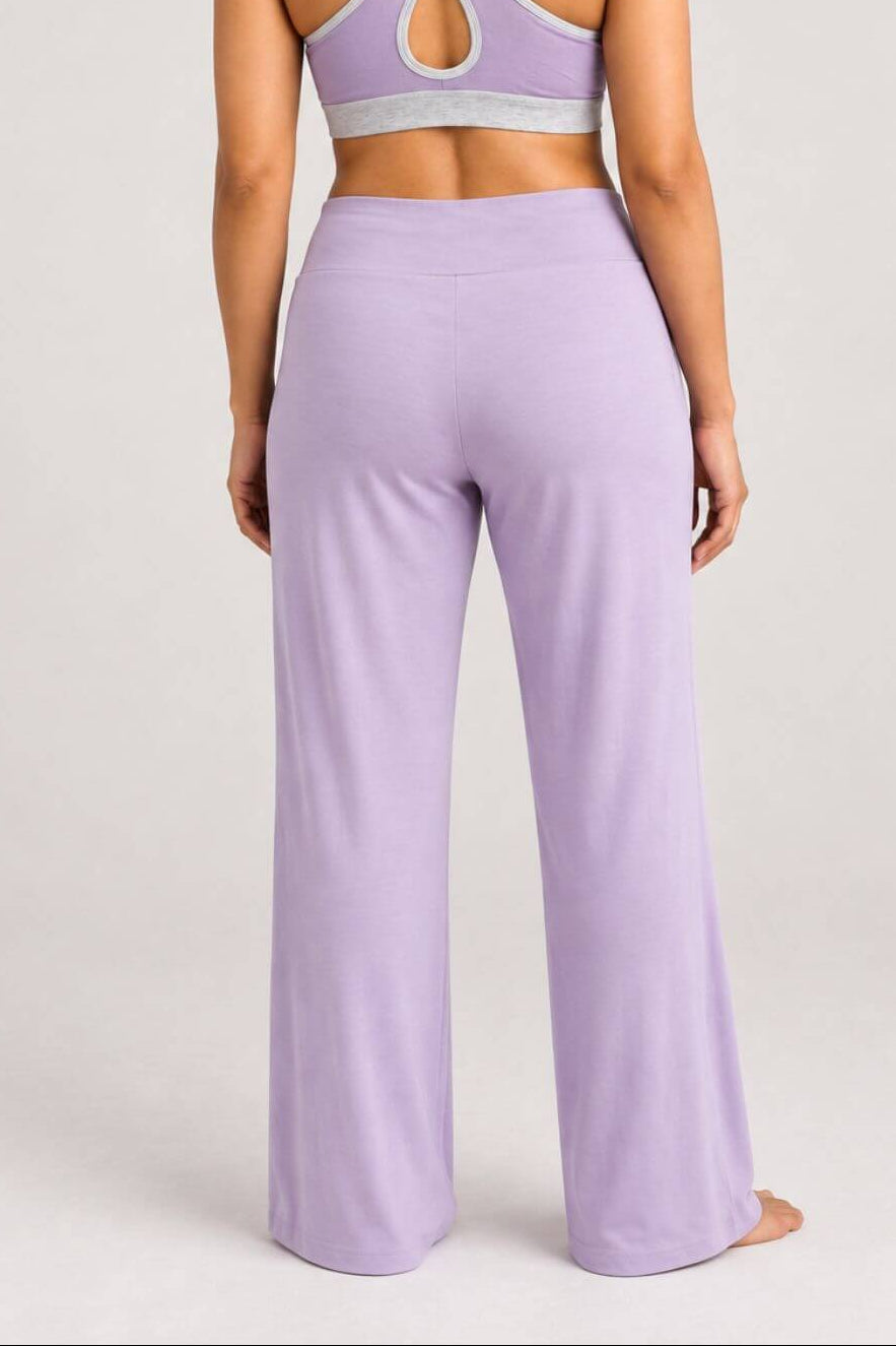 A woman shown from the back wearing a lavender two-piece activewear set consisting of a sports bra with crisscross straps and matching high-waisted wide-leg yoga pants, set against a plain light gray studio background.