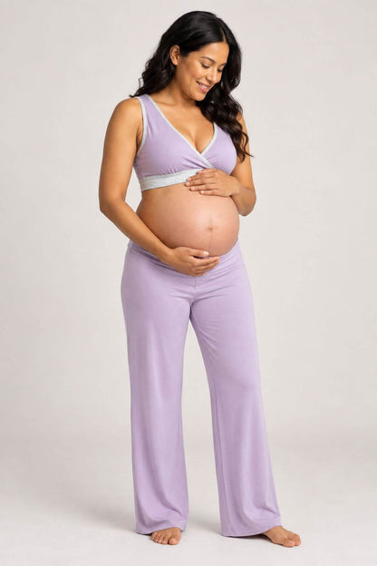 A pregnant woman wearing a light purple maternity sleep set consisting of a wrap-style tank top and matching wide-leg pants, standing against a neutral light gray studio background.