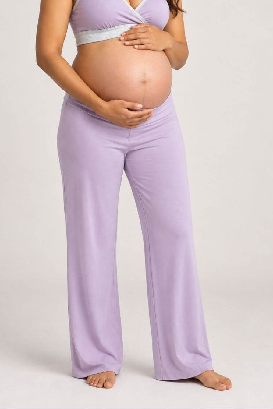 A pregnant woman wearing a light purple maternity sleep set consisting of a wrap-style tank top and matching wide-leg pants, standing against a neutral light gray studio background..