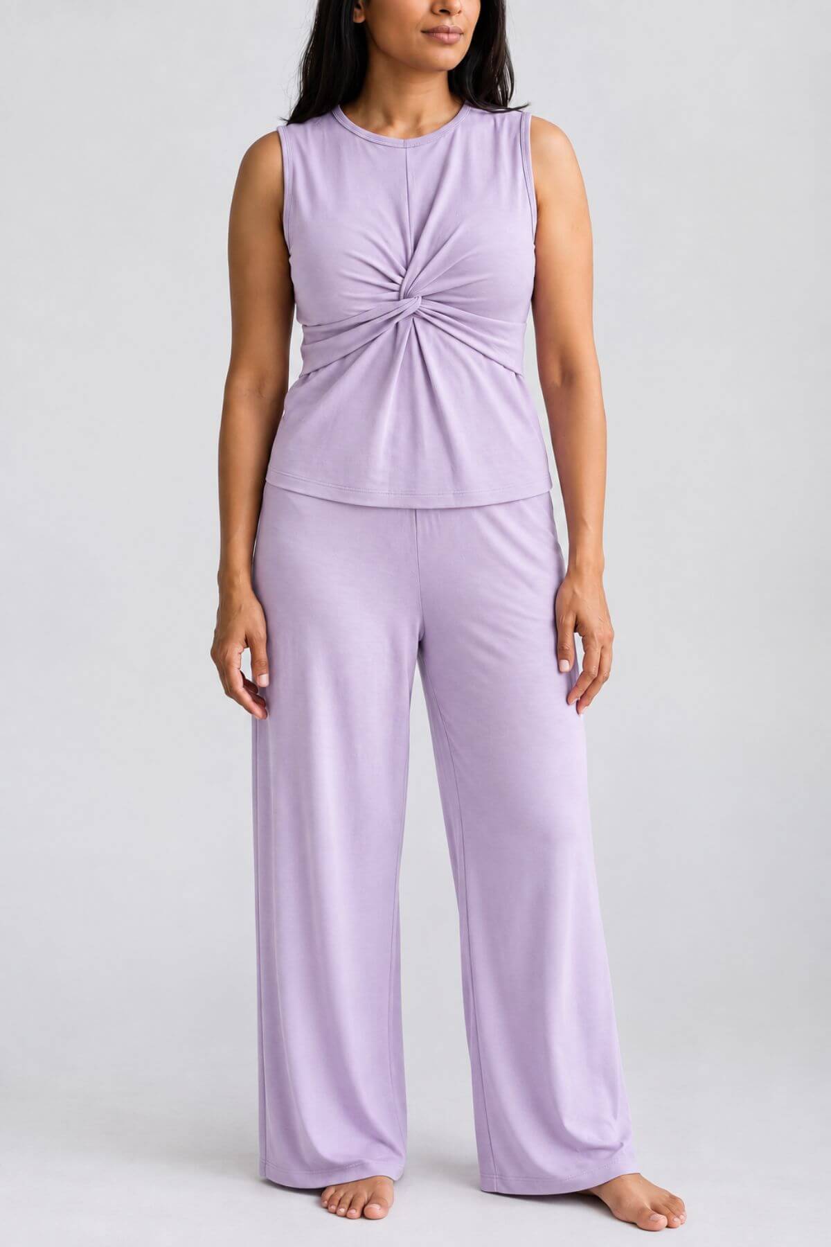 A woman modeling a lavender sleeveless knit loungewear set featuring a knotted front top and matching wide-leg pants, photographed against a neutral light gray studio background.