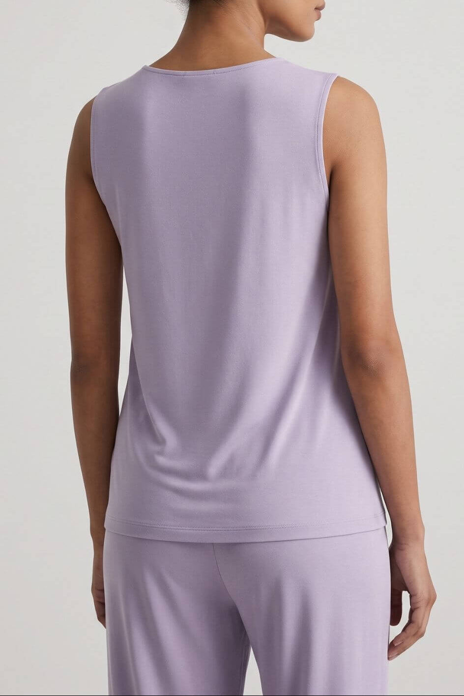 A woman shown from the back wearing a sleeveless light lavender top and matching pants against a plain light gray studio background.