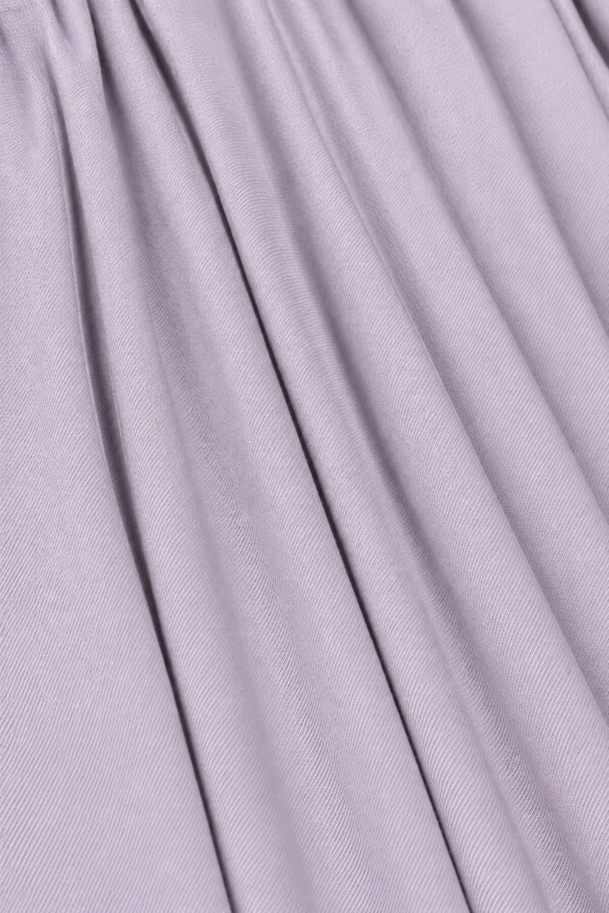 A close-up of draped lavender-gray fabric with soft vertical folds and a fine ribbed texture.