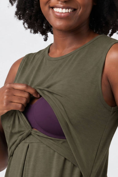 A close-up of a woman wearing an olive green sleeveless top and lifting the fabric to reveal a purple bra underneath, against a light gray background.