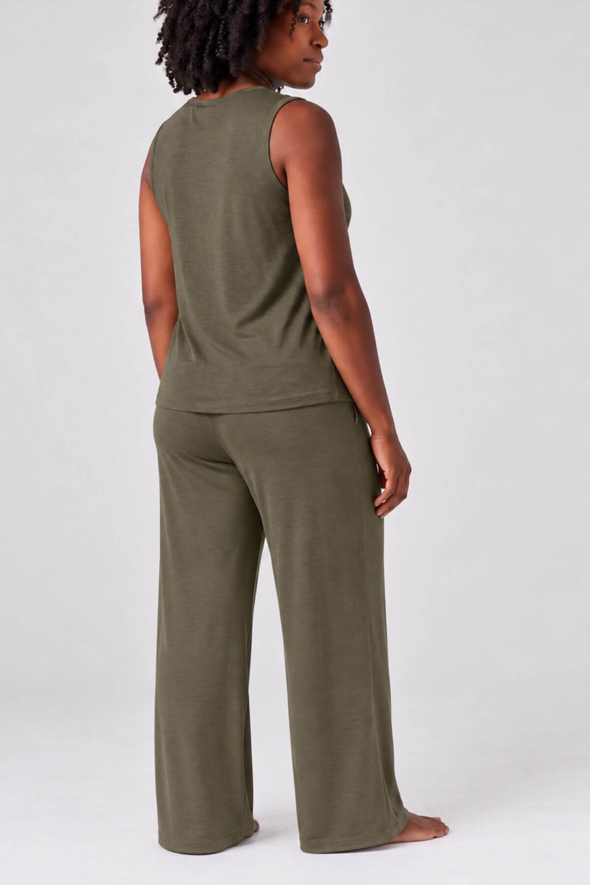 A woman shown from the back wearing an olive green sleeveless top and matching wide-leg pants against a light gray studio background.