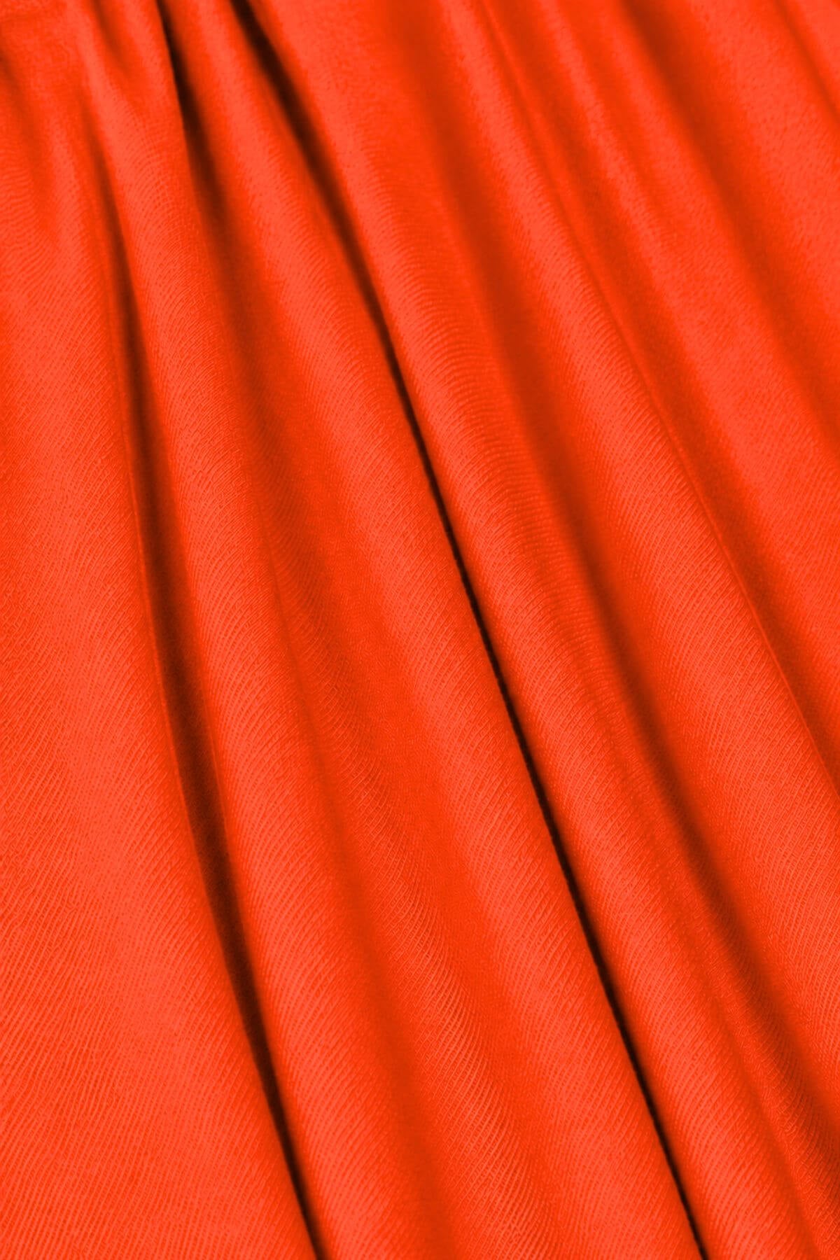 A close-up of bright orange-red fabric with soft vertical folds and a fine woven texture.