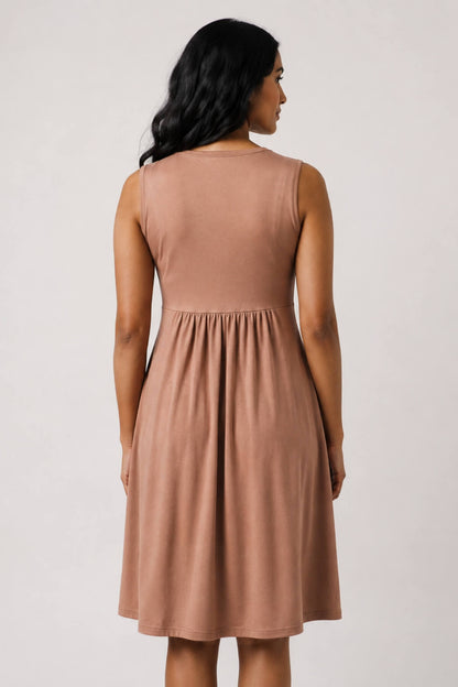 A woman shown from the back wearing a sleeveless, knee-length dusty rose dress against a plain light gray studio background.