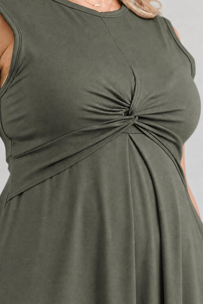 Close-up of a sleeveless olive green dress with a twisted knot detail at the waist, shown on a model against a light gray background.