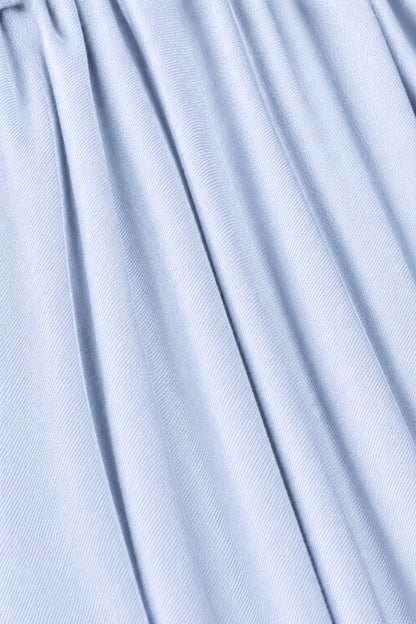 A close-up of light blue fabric with soft vertical folds and a fine ribbed texture.