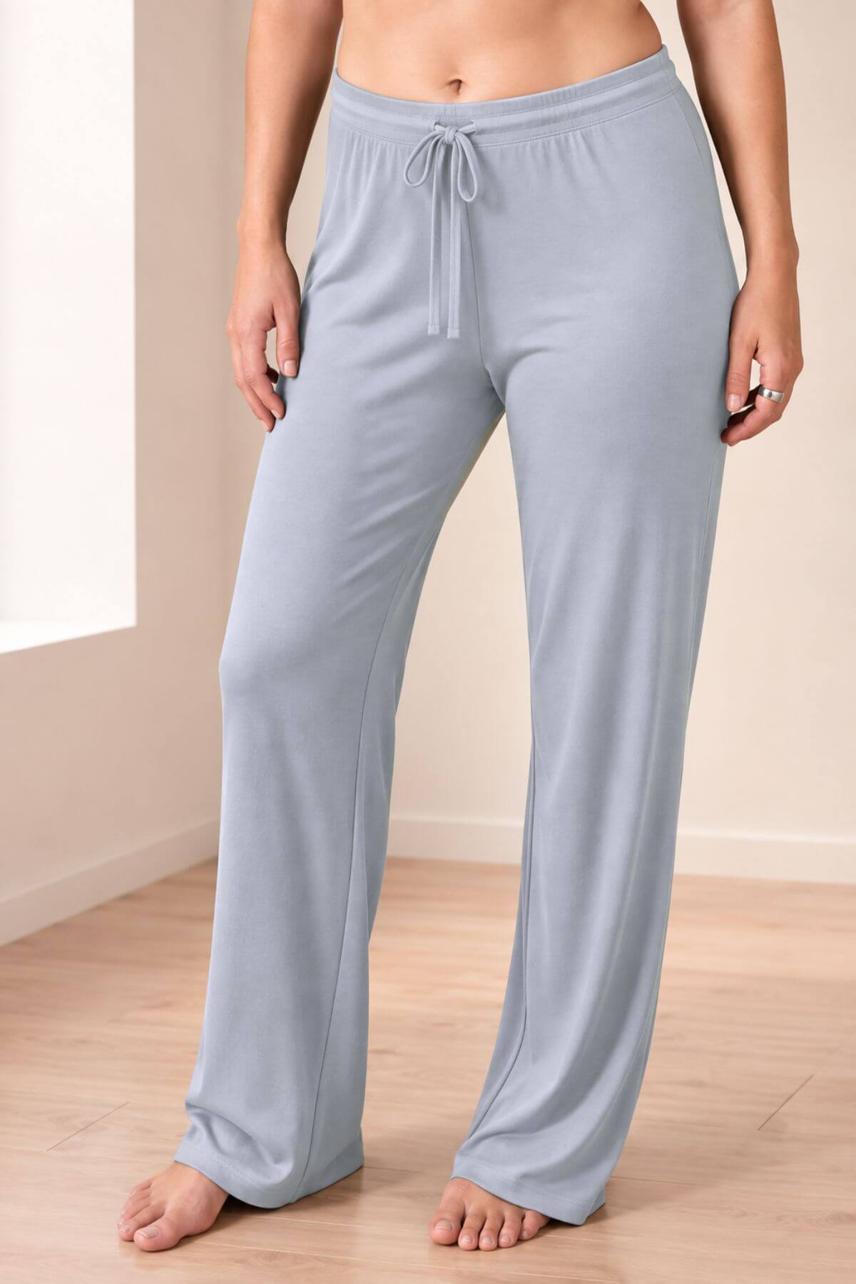 A person wearing light blue lounge pants with a drawstring waist, standing barefoot on a light wood floor in a simple indoor room.