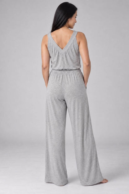 A woman shown from the back wearing a light gray sleeveless jumpsuit with a V-neckline and wide-leg pants, photographed against a plain light gray studio background.