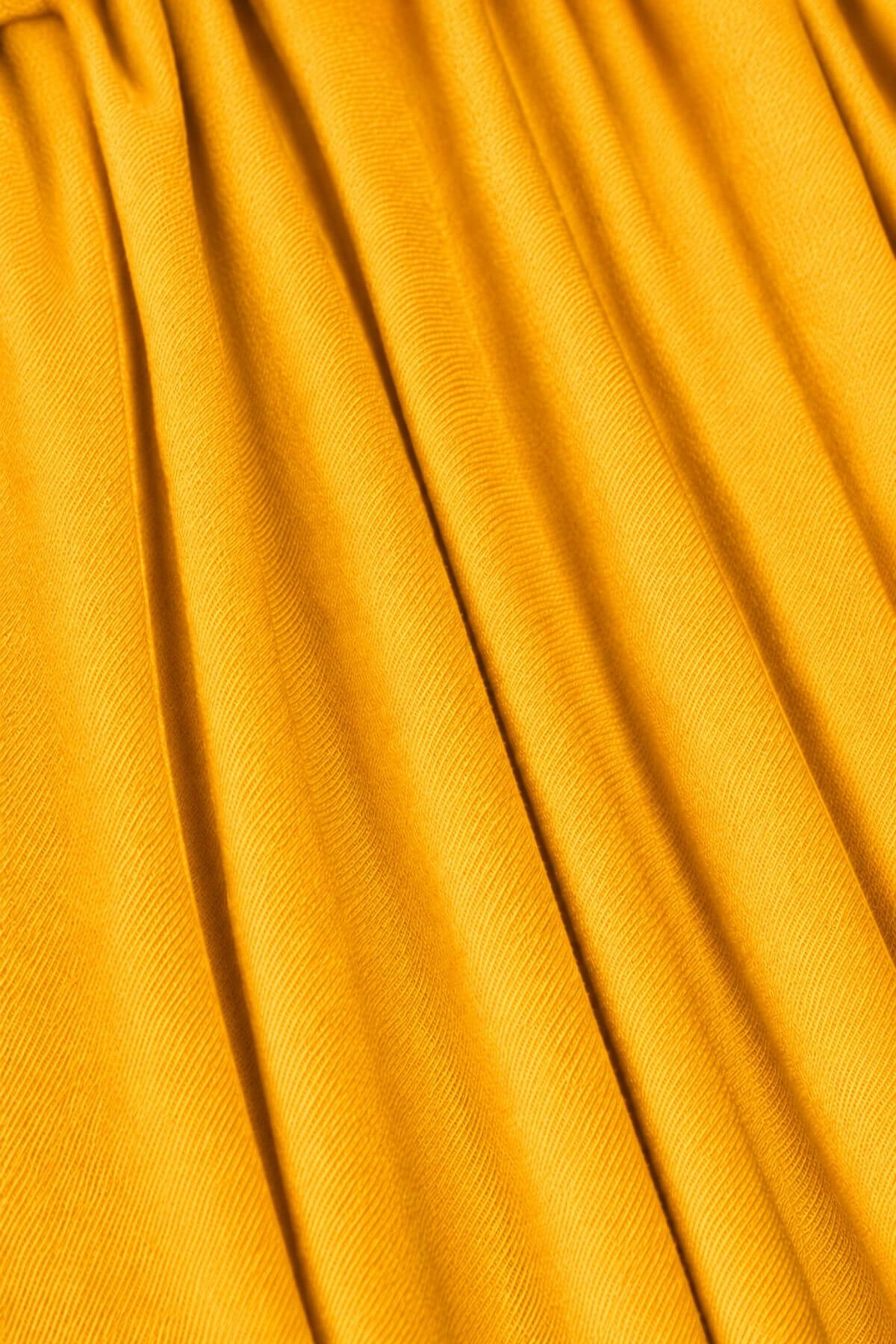 A close-up of draped mustard yellow fabric with soft vertical folds and a fine woven texture..