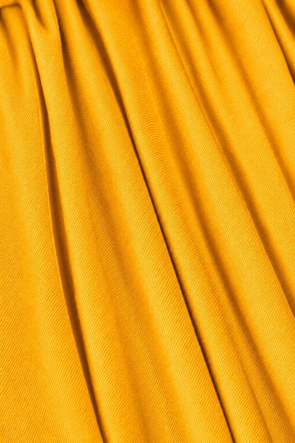 A close-up of draped mustard yellow fabric with soft vertical folds and a fine woven texture..