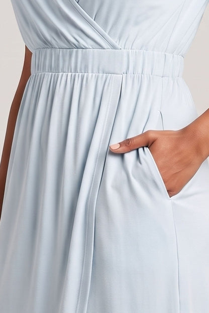 Close-up of a light blue wrap-style dress with a gathered waistband and side pocket, shown on a model with one hand in the pocket.