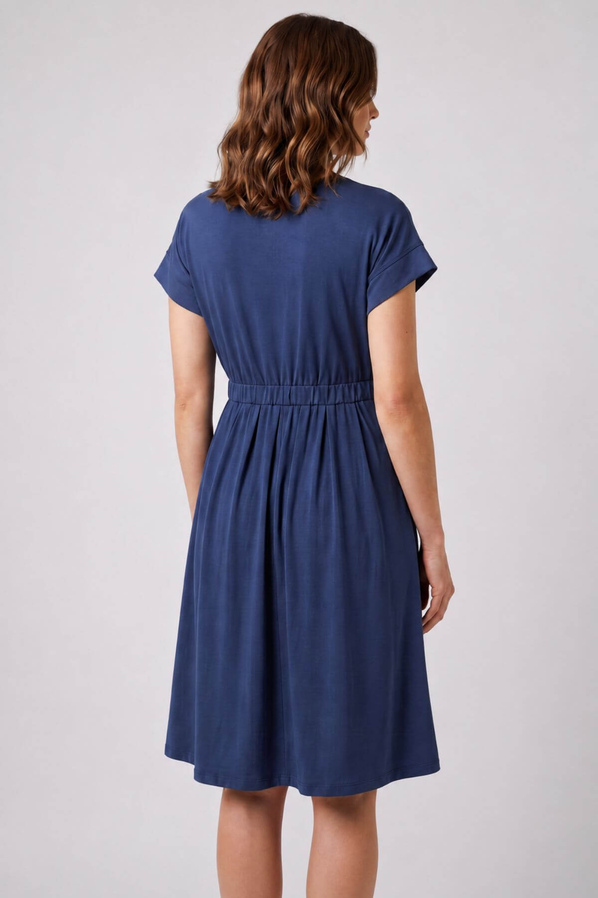 A woman viewed from the back wearing a navy blue short-sleeve dress with a gathered waist, set against a plain light gray studio background.