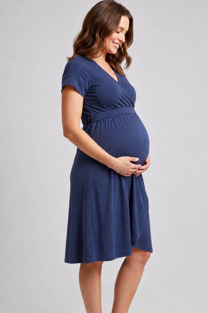 A pregnant woman wearing a short-sleeve navy blue maternity dress, standing against a light gray studio background.