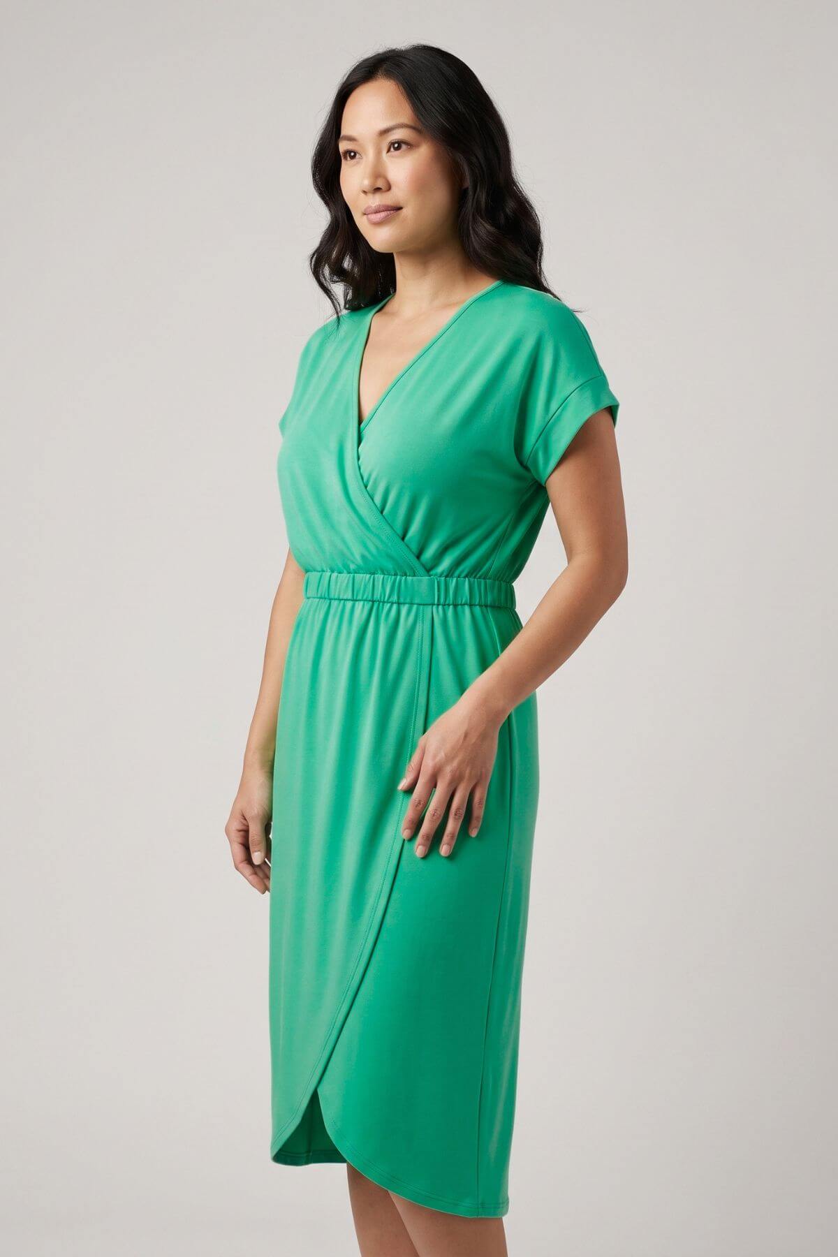 A woman modeling a bright green wrap-style midi dress with short sleeves and a V-neckline, photographed against a plain light gray studio background.