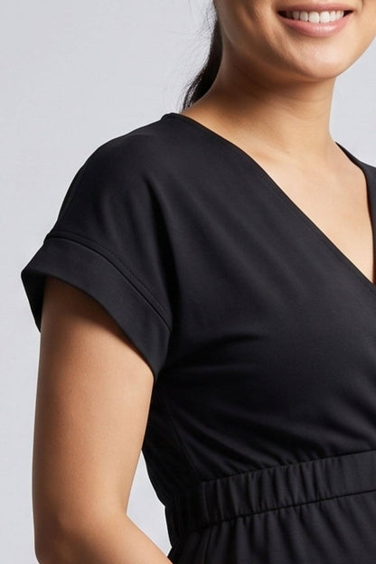 Close-up of a woman wearing a black short-sleeve V-neck dress or top with a gathered waist, shown against a light gray studio background.