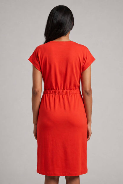 A woman viewed from the back wearing a bright red short-sleeve dress with a gathered waist, standing against a plain light gray studio background.