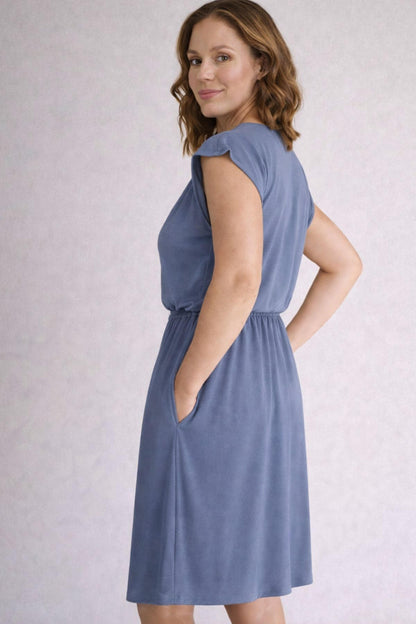 Back view of a woman wearing a gray blue nursing dress against a light gray background