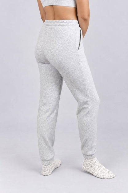 A person shown from the back wearing light heather gray jogger sweatpants with a side zipper, paired with a matching light gray crop top and white knit socks, against a plain light gray studio background.