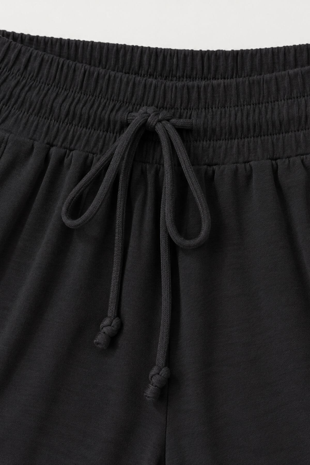 Close-up of black drawstring shorts showing the elastic waistband and cord details.