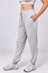 A person wearing light heather gray jogger sweatpants with an elastic drawstring waist and side pockets, paired with white athletic sneakers, against a light gray studio background.