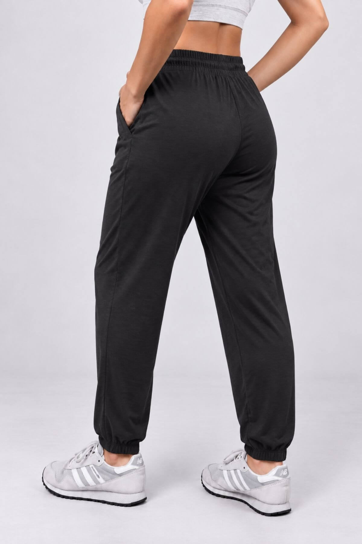 Black jogger-style pants with an elastic waistband and cuffs, shown on a model from the back against a light gray studio background.