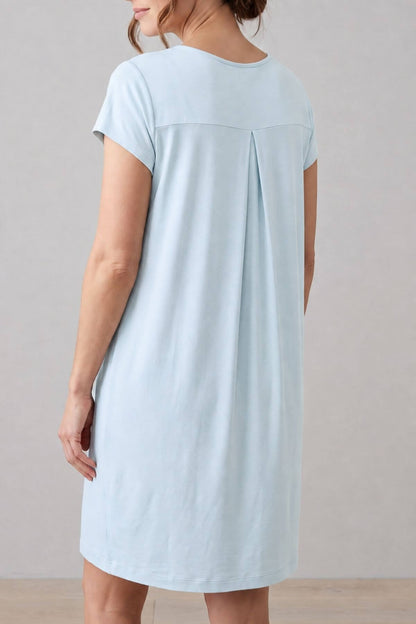 A woman wearing a light blue short-sleeve nightgown dress, shown from the back against a neutral light gray studio background.