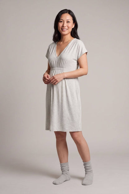 A woman modeling a light gray short-sleeve V-neck dress with a gathered waist, paired with matching gray socks, against a solid light gray studio background.