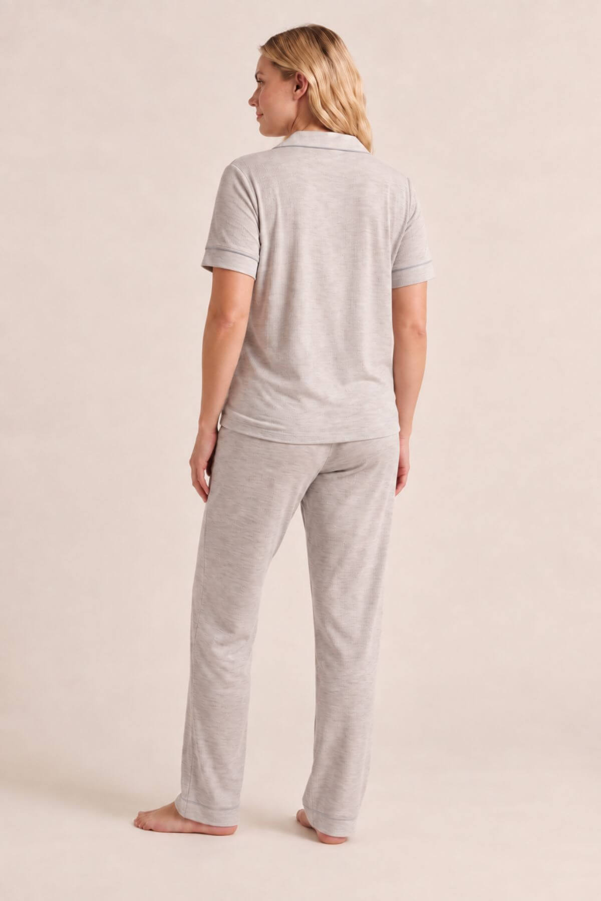 A woman wearing a light heather gray short-sleeve polo shirt and matching relaxed-fit pants, shown from the back against a plain beige studio background.