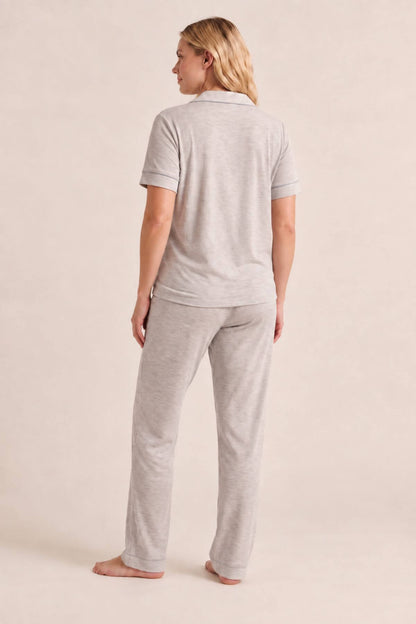 A woman wearing a light heather gray short-sleeve polo shirt and matching relaxed-fit pants, shown from the back against a plain beige studio background.
