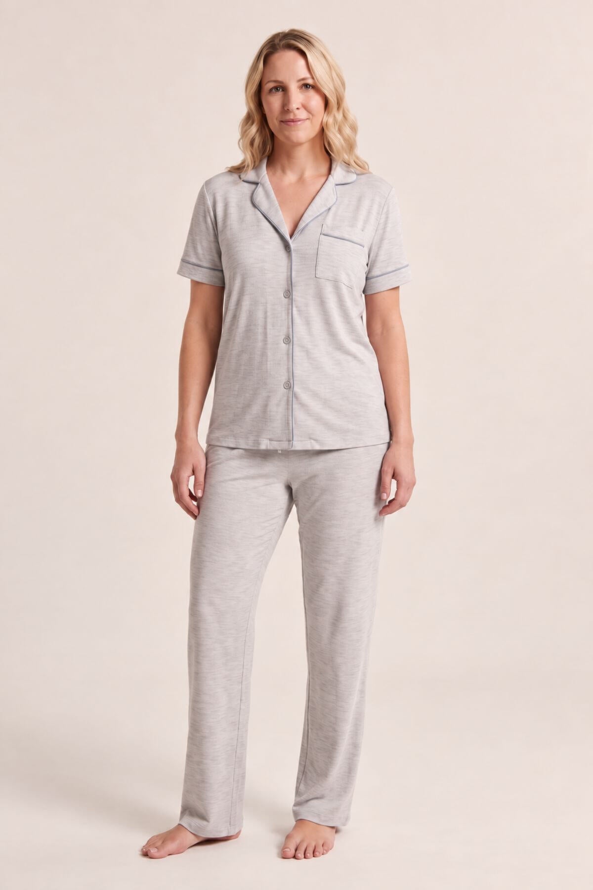 A woman modeling a light heather gray short-sleeve pajama shirt with matching pajama pants, standing against a solid light beige studio background.