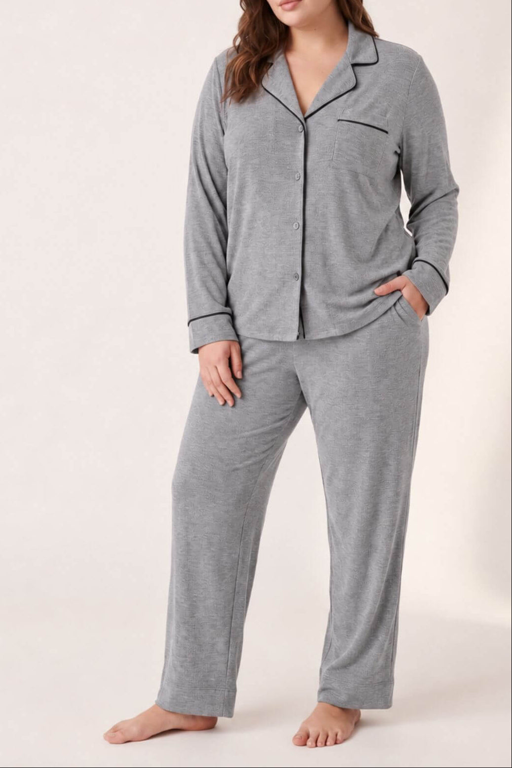 A woman modeling a heather gray two-piece pajama set with a button-front long-sleeve top and matching pants, photographed against a plain light beige studio background.