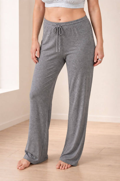 A person wearing heather gray drawstring lounge pants, shown from the waist down in a bright indoor room with light wood flooring.