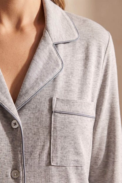 Close-up of a person wearing a light gray ribbed pajama top with contrasting dark piping, showing the collar, chest pocket, and buttons.
