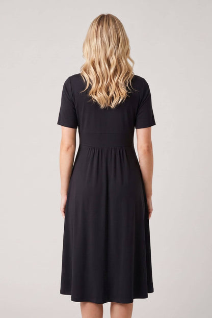 A woman viewed from the back wearing a short-sleeve black midi dress against a plain light gray studio background.
