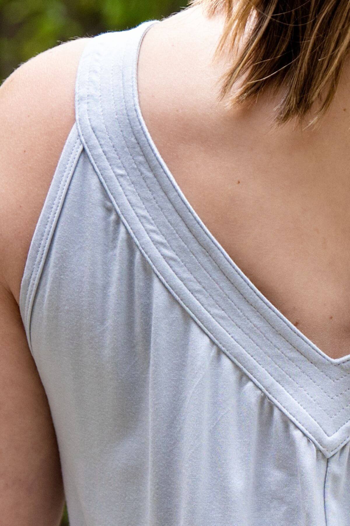 Close-up of a person wearing a light gray sleeveless top, showing the back neckline and shoulder area.
