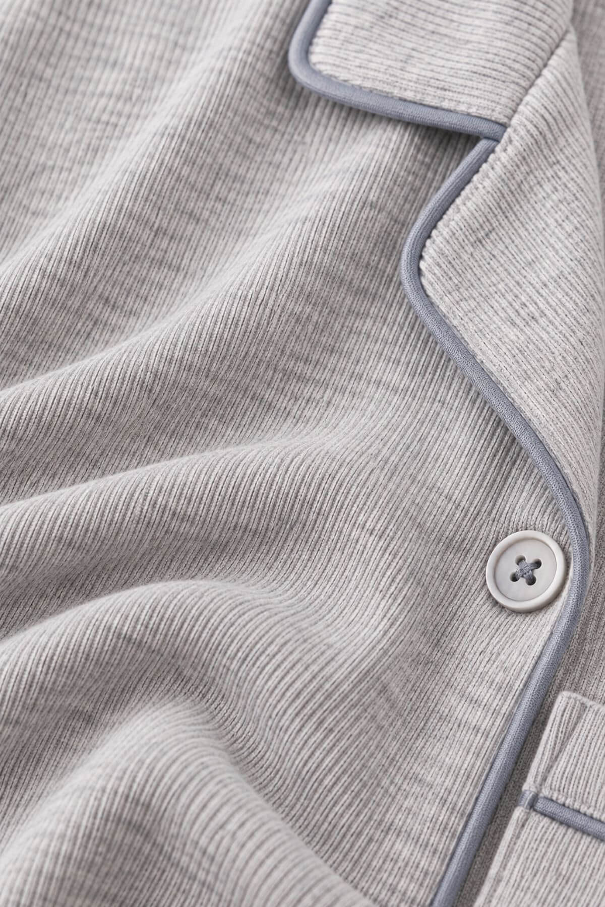 Close-up of a light gray ribbed knit pajama top with light blue-gray piping and a matching button.