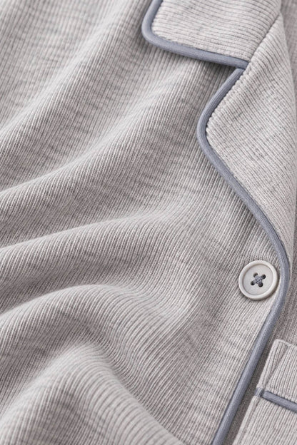 Close-up of a light gray ribbed knit pajama top with light blue-gray piping and a matching button.
