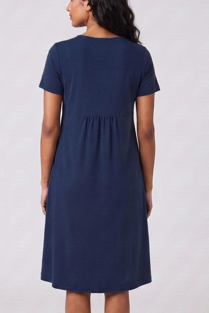 A woman wearing a short-sleeve navy blue dress, shown from the back against a light gray studio background.