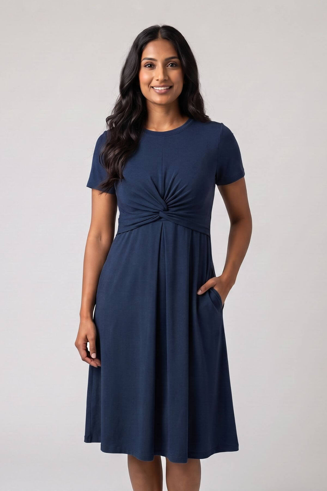 A woman modeling a navy blue short-sleeve A-line dress with a gathered twist detail at the waist and side pockets, set against a plain light gray studio background.