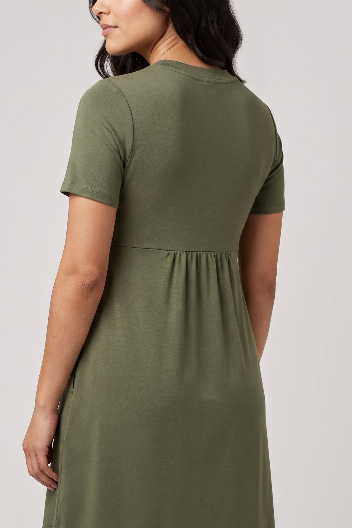 A woman wearing a short-sleeve olive green dress, shown from the back against a plain light gray studio background.
